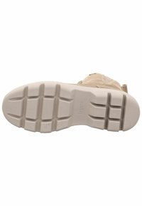 Suela texturizada en color beige claro con un patrón de relieve prominente y un logotipo estampado. Bordes lisos y contorneados que ofrecen un agarre y estabilidad de soporte.