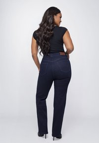 Donker gewassen, high-waisted jeans met een slim fit en achterzakken. Heeft een merknaam in een bruine leren patch op de tailleband.