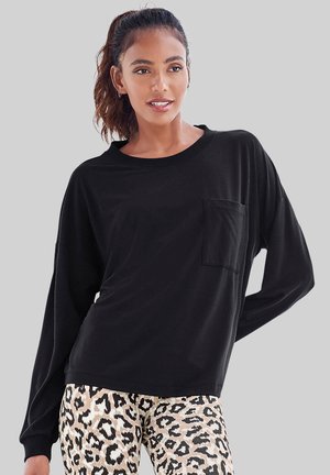 Schwarzes Langarmshirt mit Rundhalsausschnitt und Fronttasche, kombiniert mit beigen und schwarzen Leopardenmusterleggings. Glatte Textur.