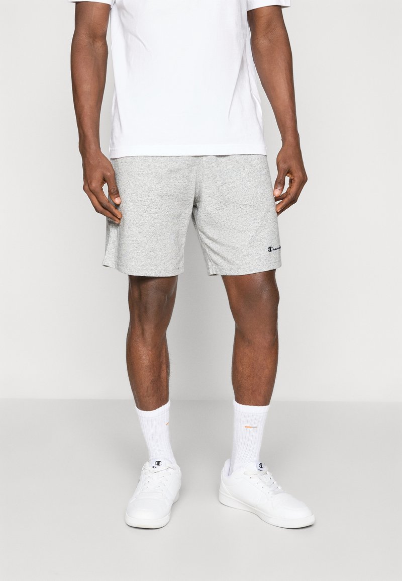 Gray athletic shorts made of cotton blend, featuring an elastic waistband and a small logo on the hem. Worn with a white t-shirt and socks.