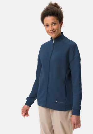 Marineblauwe zip-up jasje met een gestructureerd patroon, hoge kraag en elastische manchetten. Bevat het "Vaude" logo aan de onderzijde.