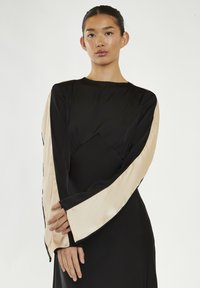 Abito nero con lunghe maniche di satin beige e un corpetto aderente con dettaglio arricciato in vita. Texture liscia con accenti a contrasto.