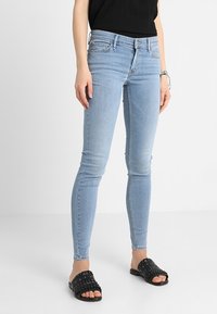 Jeans ajustados de denim en color azul claro, con un corte slim y diseño estándar de cinco bolsillos, combinados con sandalias negras tipo slide.