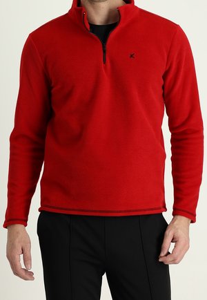 Pullover in pile rosso con colletto a zip a metà, caratterizzato da un logo nero sul petto. Texture liscia, maniche lunghe e dettagli cuciti all'orlo.
