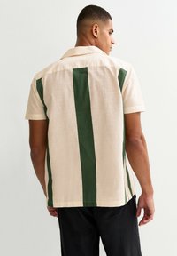 Camicia a maniche corte con strisce verticali verdi e beige. Realizzata in tessuto strutturato, presenta un colletto e un orlo dritto.