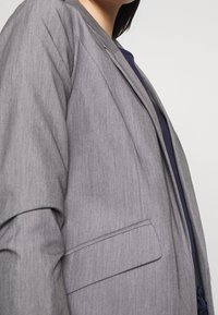 Grå kavaj med en subtil textur, en enkel ficka och öppen framtidsdesign. Har en smidig, skräddarsydd silhuett med minimal detaljering.