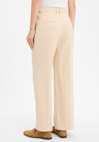 Person wearing beige wide-leg trousers and tan suede loafers, standing against a plain white background.