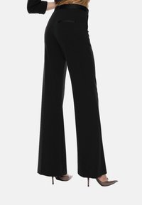 Pantaloni neri a gamba larga realizzati in tessuto morbido, con una cintura elegante e una tasca posteriore. Abbinati a scarpe con tacco alto.