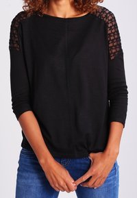 Zwarte lange mouw top met kanten accenten op de schouders, ronde halslijn en een relaxte pasvorm. Gecombineerd met blauwe jeans, heeft een zachte textuur.
