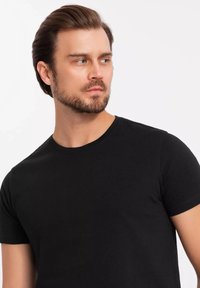 Černé bavlněné tričko s krátkým rukávem ve stylu crew neck, s klasickým střihem a hladkou texturou, zobrazené na mužském modelu na jednolitém pozadí.