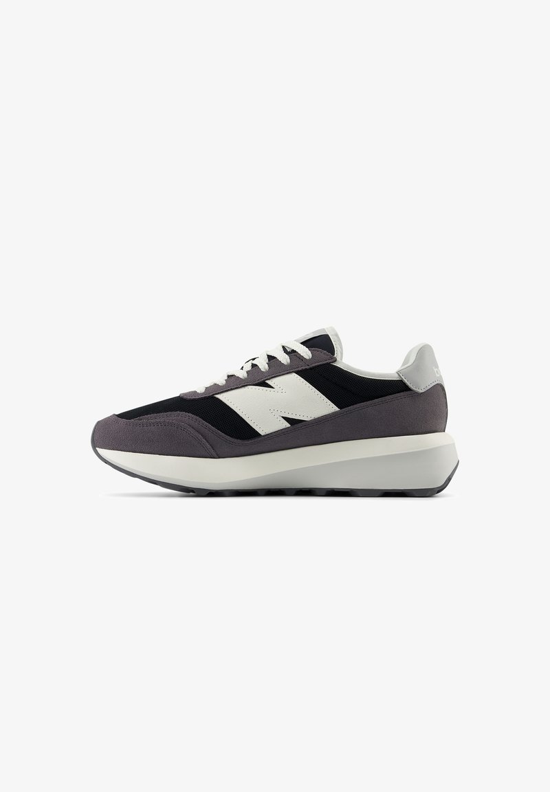 Sportliche Schuhe mit einem schwarzen Mesh-Obermaterial, grauen Wildlederakzenten, weißem Logo und einer dicken weißen Zwischensohle. Strukturiertes Gummiprofil für besseren Halt.