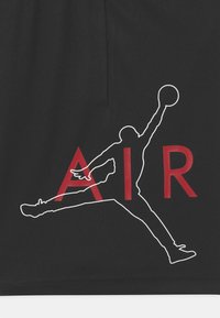 Svart tyg med en vit silhuett av en hoppande figur och röd text som stavar "AIR", vilket framhäver sportig design och kontrast.