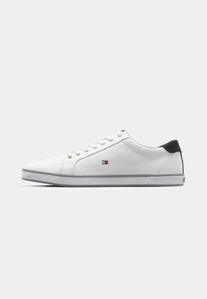Witte sneakers met een gladde textuur, voorzien van een zwarte hielaccent, veters en een klein logo in rood, wit en blauw aan de zijkant.
