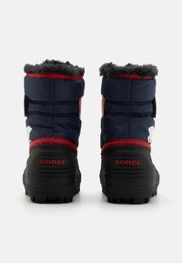 Marine isolierte Stiefel mit grauem Fellfutter und roten Akzenten. Texturierte schwarze Gummisohle und Sorel-Branding auf der Rückseite.