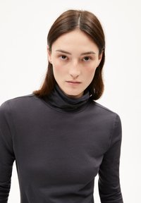 Marineblaue Rollkragenoberteil aus weichem, dehnbarem Stoff mit langen Ärmeln und schmaler Silhouette. Glatte Textur, minimales Design und keine sichtbaren Muster.