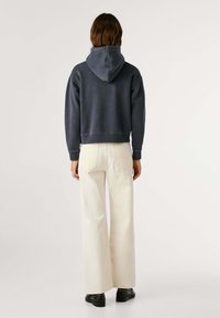 Felpa con cappuccio di colore blu navy con un design corto, con polsini e bordo a costine. Abbinata a pantaloni larghi color crema e scarpe nere.