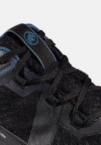 Sort sportsko med mesh og syntetiske materialer, med mørke snørebånd, en tekstureret overflade og et logo på tungen.
