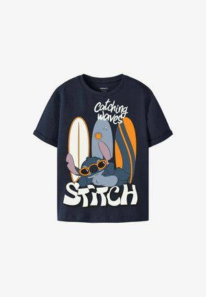 T-shirt bleu marine avec le personnage de dessin animé Stitch portant des lunettes de soleil orange, se détendant devant trois planches de surf et le texte « Catching waves ».