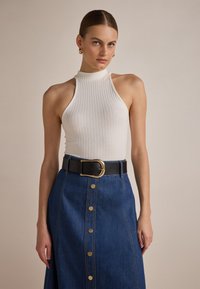 Witte geribbelde haltertop gecombineerd met een high-waisted blauwe denimrok met gouden knopen en een zwarte riem met een gouden gesp.