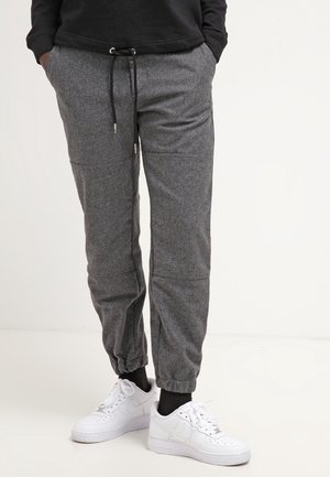 Person wearing grey sweatpants with elastic cuffs and black drawstring, paired with white sneakers against a light background.