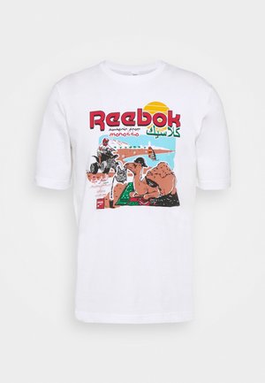 Biała koszulka Reebok z kolorową grafiką wielbłąda, quadowca, krajobrazu pustyni oraz tekstem „souvenir from Morocco” po angielsku i arabsku.