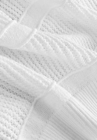 Gros plan d'un tissu tricoté blanc avec des motifs texturés variés et des sections côtelées.