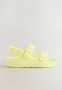 Sandale jaune clair à bout ouvert avec deux brides à boucle réglables et une bride arrière, semelle texturée pour une meilleure adhérence, présentée sur un fond blanc.