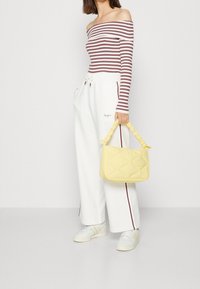 Top a righe bianco e bordeaux, abbinate a pantaloni bianchi a gamba larga con una striscia rossa, mentre tiene una borsa a tracolla gialla trapuntata.