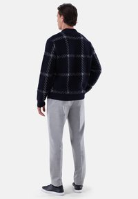 Dunkelblau gestrickter Pullover mit kariertem Muster, kombiniert mit hellgrauen Hosen und schwarzen Sneakers, von hinten betrachtet.