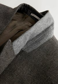 Dark brown textured coat with raised grey felt collar showing patterned inner lining and a small fabric label inside the neck.