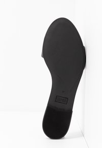 Semelle de chaussure noire avec une finition lisse, légèrement texturée. Présente une forme arrondie et un détail de marque. Taille indiquée : 37.