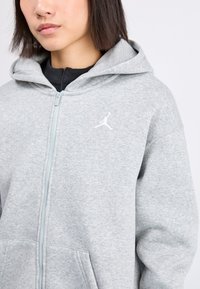 Szürke, zipzárral záródó kapucnis felső, amely textúrált anyagból készült, elöl kissé kanguru zsebbel és fehér Jumpman logóval a bal mellrészen.