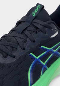 Marine atletisk sko med teksturert mesh-overdel, grønne og blå aksenter, med intrikate overlegg, runde snørebånd og polstret krage.