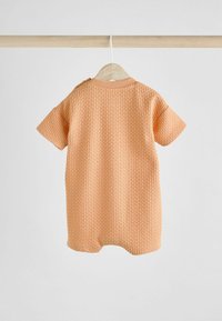 Pfirsichfarbener Babystrampler mit kurzen Ärmeln, strukturiertem Waffelmuster, Rundhalsausschnitt und Druckknöpfen an einer Schulter.