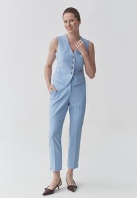Světle modrá obleková vesta s pěti knoflíky, doplněná o úzké kalhoty ve stejném odstínu. Obsahuje elegantní design a boty na podpatku s špičatou špičkou.