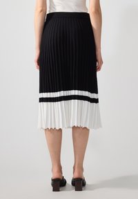 Zwart-wit geplooide midi-rok met een geribbelde textuur, voorzien van een contrasterende witte band aan de onderkant en een soepele tailleband.