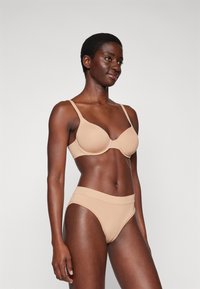 Beige naadloze beha met verstelbare bandjes en een gladde afwerking, gecombineerd met bijpassende hoge taille slips, beide met een comfortabele pasvorm.