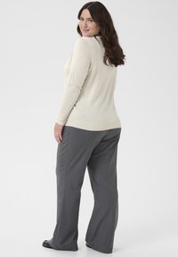 Pulover bej deschis cu mâneci lungi, tricotat texturat și tiv cu nervuri, asortat cu pantaloni gri, largi și pantofi negri.