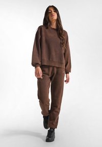 Felpa marrone e pantaloni abbinati realizzati in tessuto morbido. La felpa ha una vestibilità comoda con polsini a coste, e i pantaloni sono a gamba dritta con tasche laterali.