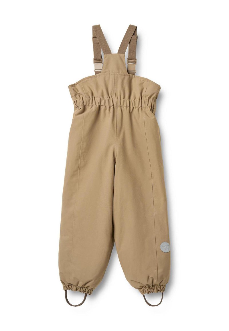 Salopette imperméable beige avec bretelles réglables, taille élastique et chevilles resserrées. Présente un logo circulaire sur la jambe gauche.