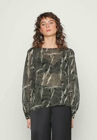 Blusa preta e creme com padrão abstrato ondulado, mangas longas e decote redondo, feita de tecido leve e ligeiramente transparente.