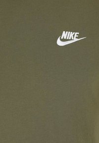 T-shirt in cotone verde oliva con logo Nike ricamato in bianco sul lato sinistro in alto. Texture liscia, design semplice.