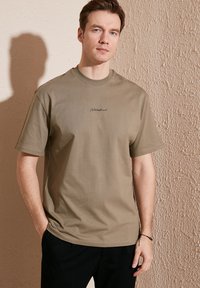 Olivengrøn kortærmet t-shirt med rund hals og broderet logo på brystet; blødt, ensfarvet stof med en afslappet pasform og uden mønstre.