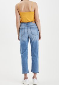 Yellow spaghetti strap top paired with light blue mom jeans featuring a relaxed fit, four pockets, and rolled hems. Worn with white sneakers.