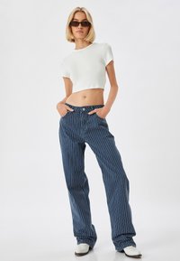 Blauw gestreepte, wijde jeansbroek met een knoopsluiting en zakken. Gecombineerd met een korte witte crop-top en witte schoenen.