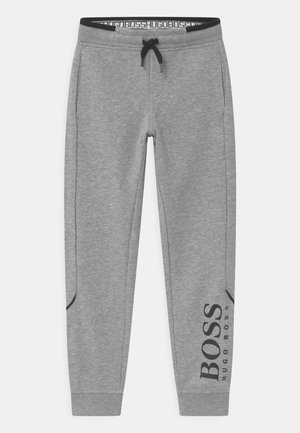 Grijze sweatpants met een zwarte elastische tailleband, een trekkoord, zijzakken en een logo op het linkerpant. Gladde textuur.