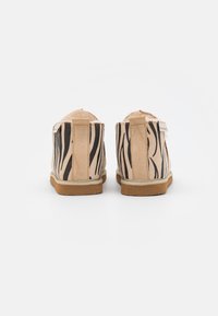 Stivali alla caviglia color beige chiaro realizzati in suede con motivi a zebra neri, dotati di un retro arrotondato, suole in gomma beige e linguette per facilitarne l'indossamento.