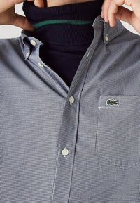 Kauluksellinen paita mustavalkoisella ruutukuviolla, yhdistetty laivastonsiniseen poolopaitaan, jossa on vihreä raita kauluksessa.