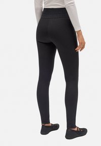 Leggings negros con una cinturilla alta acanalada, textura suave, ajuste slim y combinados con zapatos planos negros. Presenta costuras laterales sutiles.
