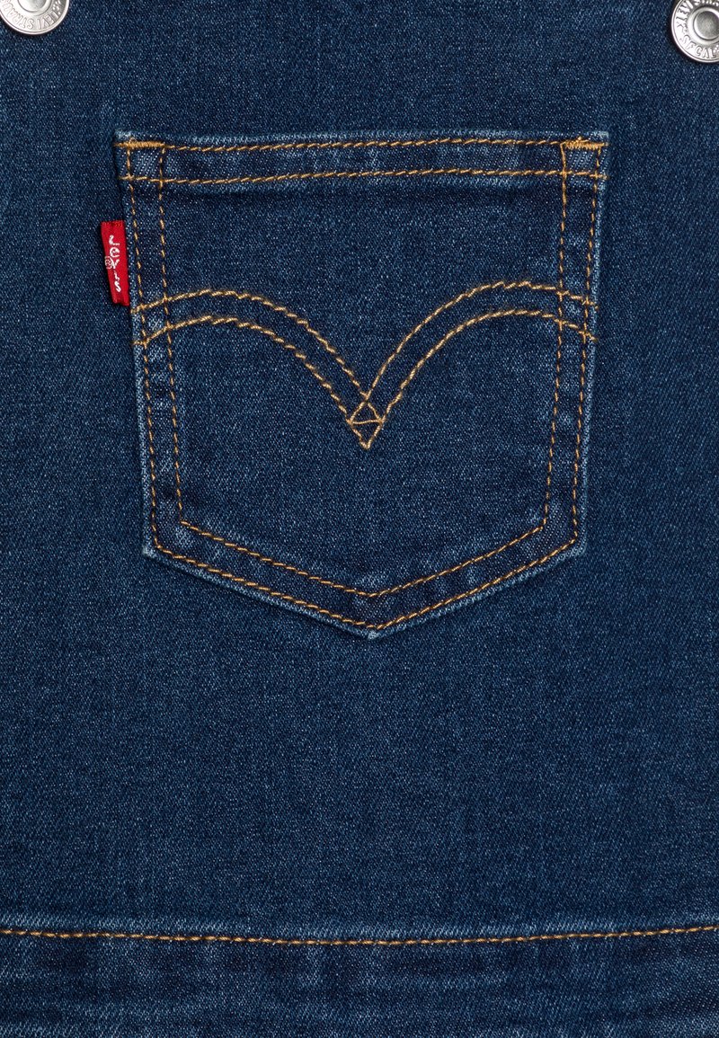 Dunkelblauer Denimstoff mit orangen Nähten. Enthält ikonisches, geschwungenes Design und ein rotes Etikett an der Seite. Silberner Knopf oben.